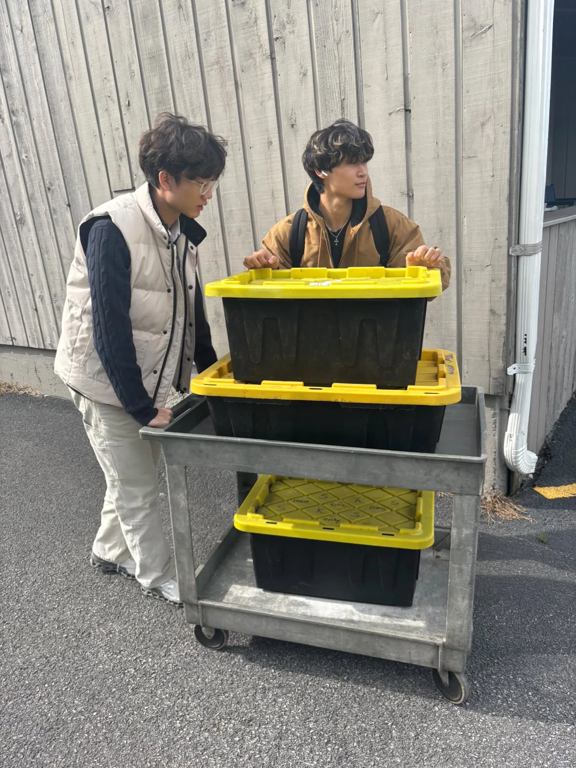 Two people stand beside a wheeled cart of black food-scrap bins with yellow lids.